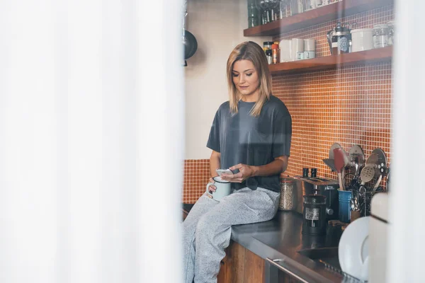 Mujer usando el teléfono celular mientras está sentado en el mostrador — Foto de Stock