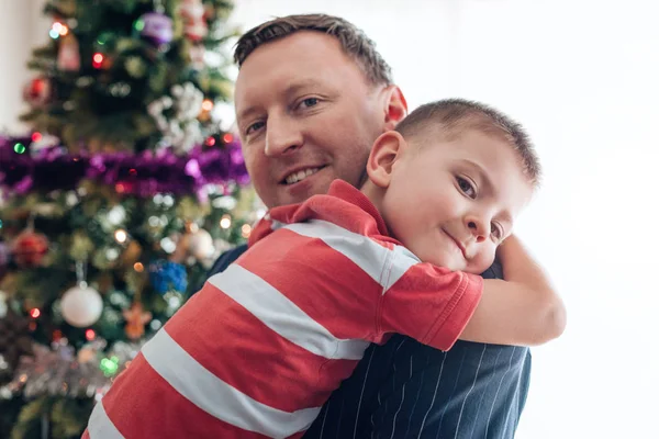 Father hugging son in front of Christmas tree — Stock Photo, Image