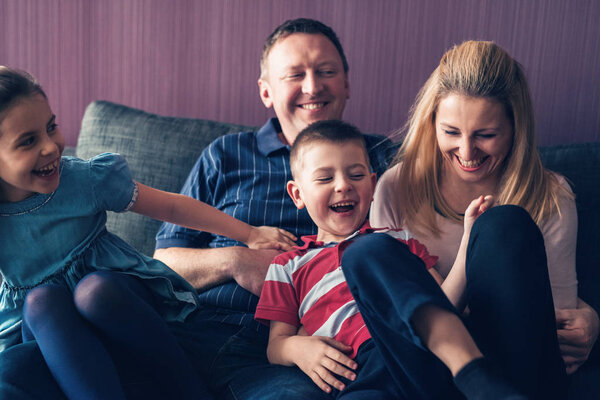 mother and father with laughing children on sofa