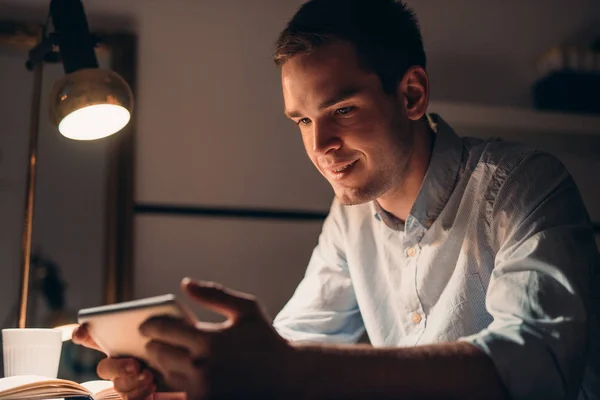 Lachende jonge zakenman met behulp van een tablet laat in de avond — Stockfoto