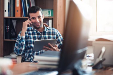 tablet kullanma ve telefonla konuşan bir adam