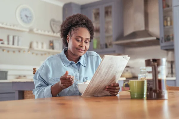 Mujer leyendo el periódico y comiendo — Foto de Stock