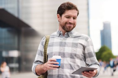 Şehir sokak bardak kahve üzerinde duran ve dijital tablet kullanarak genç adam gülümseyen