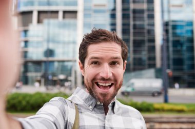 Gülümseyen ve şehirde gün dışarı çıkarırken selfies alarak sakallı neşeli genç adam