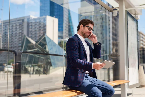 Jovem Empresário Sentado Banco Cidade Conversando Seu Celular Usando Tablet — Fotografia de Stock