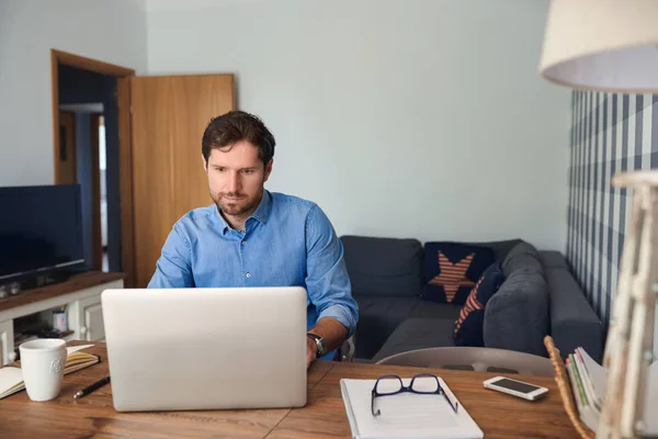 年轻人独自在家工作时 在他的起居室里在桌上用笔记本电脑上网 — 图库照片