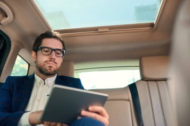 Şehrin içinden tahrik ederken dijital tablet üzerinde çalışan arabanın arka koltuğunda oturan genç işadamı odaklı