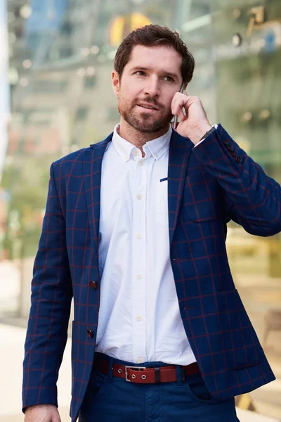 スーツだけで都市を通って歩いている間彼の携帯電話の会話に成功した青年実業家 — ストック写真