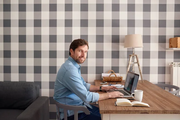 自信を持って若い男が自宅で一人で仕事しながら彼のリビング ルームのテーブルでノート パソコンでオンライン作業 — ストック写真