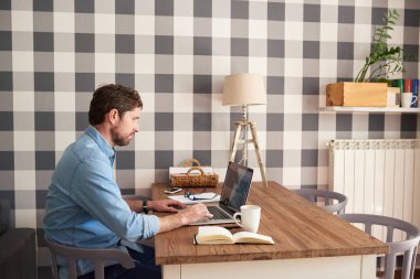 Genç adam tek başına evde online laptop ile masada oturma odasını çalışan odaklı