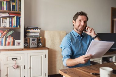 Telefonda konuşmak ve evden çalışırken evrak okuma onun oturma odasında masada oturan gülümseyen genç adam