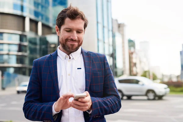 Joven Hombre Negocios Sonriente Usando Chaqueta Pie Ciudad Enviando Mensajes —  Fotos de Stock