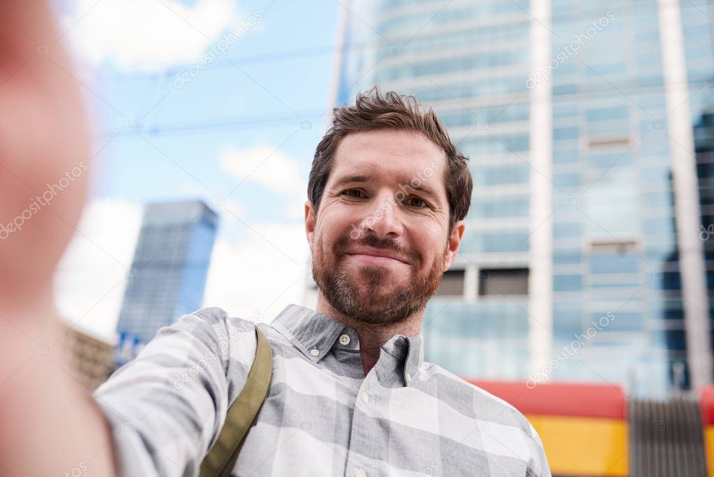 Smiling young man with beard taking selfie while enjoying day out in the city