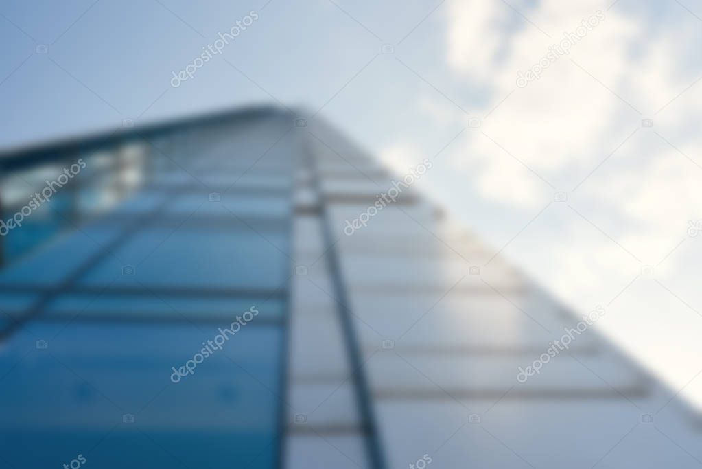 Defocused image of exterior of modern glass skyscraper rising up to the sky in the financial district of city