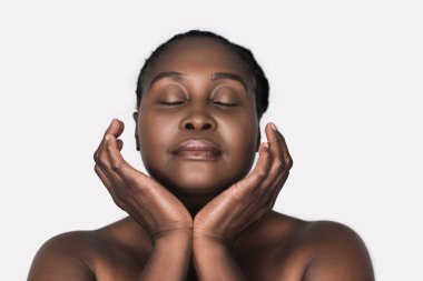 Gözleri kapalı ve elleri beyaz bir arka plan karşı yüzünü çerçeveleme ile bir mükemmel cilt konumu olan Afrikalı kadın genç artı boyutu