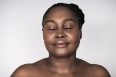 Gri bir arka plan karşı kapalı gözleri ile mükemmel cilt konumu olan Afrikalı kadın genç artı boyutu