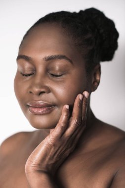 Boyutu mükemmel deri ayakta elleri yanak ve göz ile Afrikalı kadın beyaz bir arka plan karşı kapalı.
