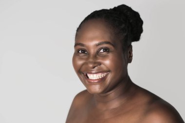 Gri bir arka plan karşı tek başına duran güzel ten rengi ile gülümseyen boyutu Afrika kadın