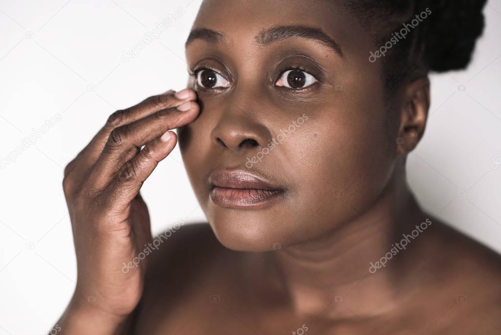 Young plus size African woman with a perfect complexion touching the skin around her eye while standing against a white background 