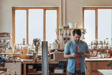 Arayan yetenekli genç woodworker atölyesinde marangozluk araçları dijital tablet kullanma dolu tek başına duran odaklı