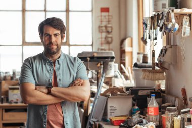 Kendine güvenen genç woodworker kollarını workbench araçları onun marangozluk atölye dolu tarafından çarpı işareti ile ayakta portresi 