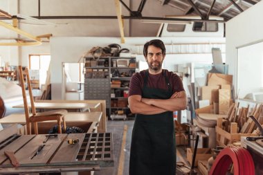 Yetenekli genç woodworker sakallı portresi, güvenle tezgah tarafından geçti kollarını ile ayakta atölyesinde marangozluk donatımın tam gördüm.