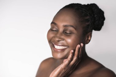 Afrikalı kadın gözleri ile ayakta yanağı dokunmadan beyaz bir arka plan karşı kapalı boyutu artı genç gülümseyen