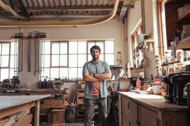 Kendine güvenen genç woodworker kollarını workbench araçları onun marangozluk atölye dolu tarafından çarpı işareti ile ayakta portresi 