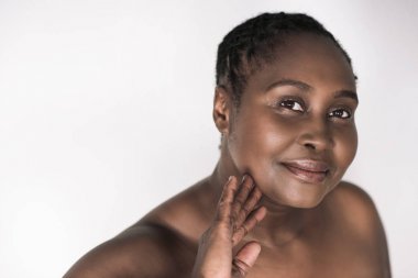 Gülümseyen genç artı boyutu Afrikalı kadın beyaz bir arka plan karşısında dururken onu güzel cilt dokunmadan