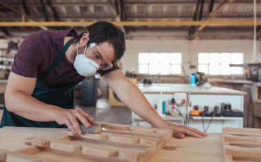 Yetenekli genç woodworker koruyucu maske ve gözlük el bir Ağaç zımparalama adet yalnız büyük atölyesinde çalışırken