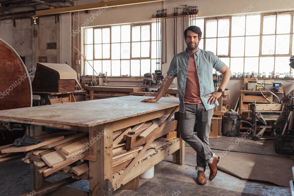 Portrait of a confident young woodworker standing next to a workbench full of wood in his carpentry workshop 