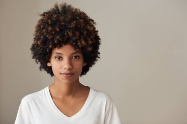 Bir sakin görünümlü genç Afrikalı kadın bir afro ve doğal cilt ayakta gri bir arka plan ile portresi