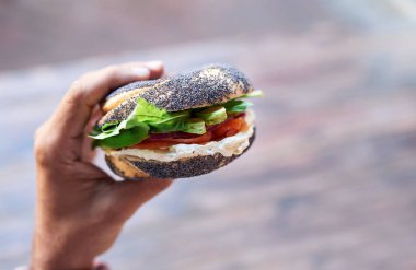 POV ayakta dışında bir lezzetli krem peynir ve somon haşhaş tohumu çörek yemek bir adamın elinde