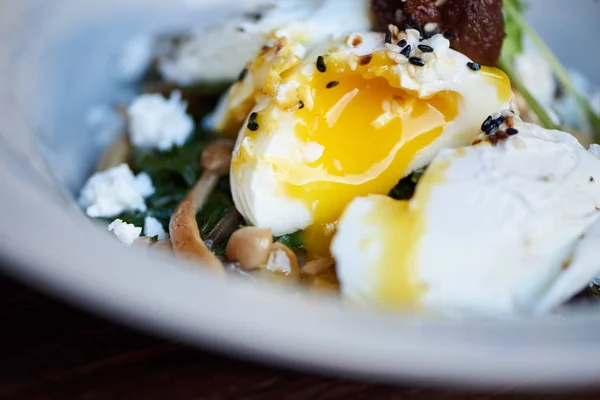 两个美味的荷包蛋 流着蛋黄 煎蘑菇 羊乳酪和混合蔬菜在桌上的碗里 — 图库照片