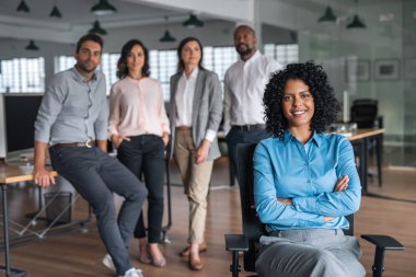 Ofis koltuğunda kollarını kavuşturarak oturan gülümseyen bir iş kadınının portresi.