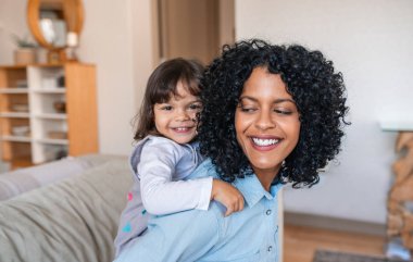 Gülümseyen anne, evdeki oturma odalarında oynarken sevimli küçük kızını sırtında taşıyor.
