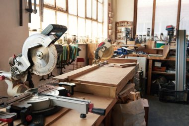Mitre testere, ahşap ve çeşitli aletler büyük bir marangozhanenin çalışma tezgahlarında oturuyor.