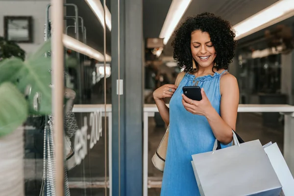 Sorrindo jovem mulher lendo um texto de celular enquanto fora de compras — Fotografia de Stock