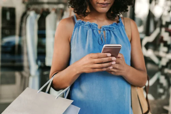 Жінка використовує свій мобільний телефон під час покупки одягу — стокове фото