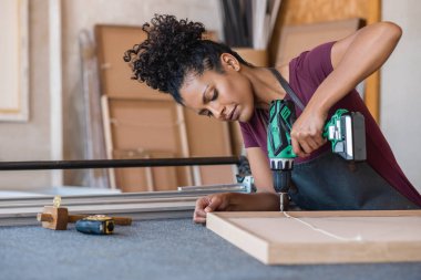 Young woman assembling a canvas frame using a drill while working at a bench in her picture framing studio