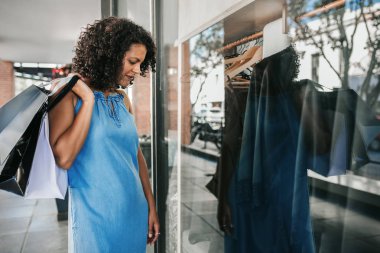 Smiling woman standing on a sidewalk and looking at the window display of a clothing store while out shopping