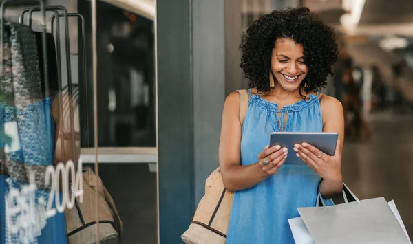 Sorrindo Jovem Mulher Carregando Sacos Olhando Para Algo Seu Tablet — Fotografia de Stock