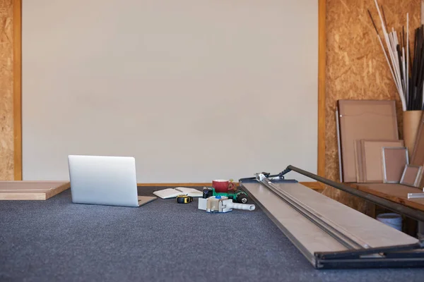 Mat cutter, laptop and a variety of wooden picture frames on a table inside of a framing workshop