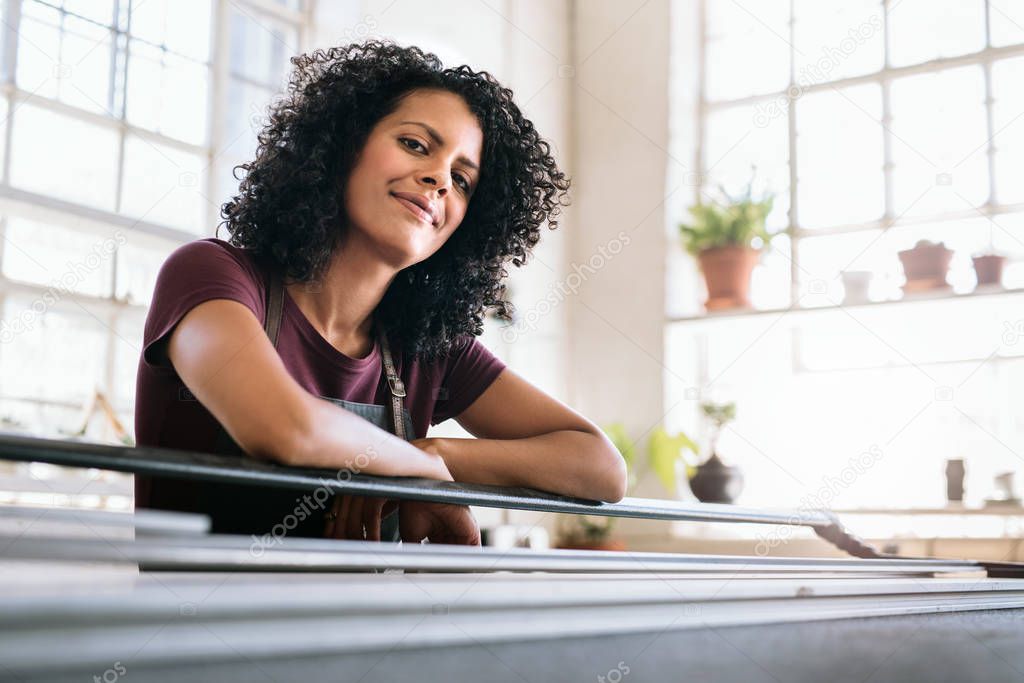 Portrait of a smiling young woman leaning against a mat cutter on a table in her picture framing studio