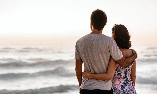 夕日を眺めながら海の地平線を眺めながら腕を組んで立っている若いカップルの愛情深い眺め — ストック写真