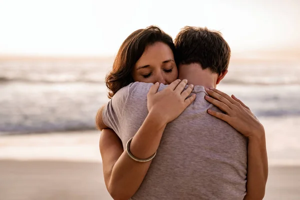 夕暮れ時に砂浜に一緒に立っている間に彼女の目を閉じて彼女の夫を抱きしめる若い女性を愛し — ストック写真