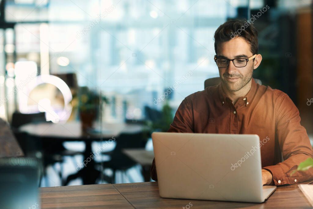 Businessman working online with a laptop while sitting at his desk in an office after hours