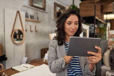 Gülümseyen genç Asyalı kadın şık butiğinin önünde dikiliyor ve dijital tablet kullanıyor.