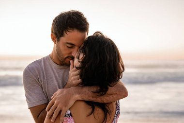 Romantik genç çift, alacakaranlıkta bir kumsalda gözleri kapalı birbirlerine bakıyorlar.