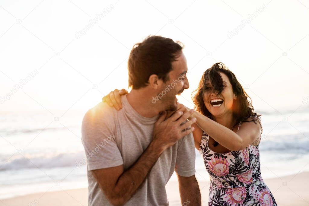 Laughing young woman and her husband having a fun day together on a sandy beach at sunset